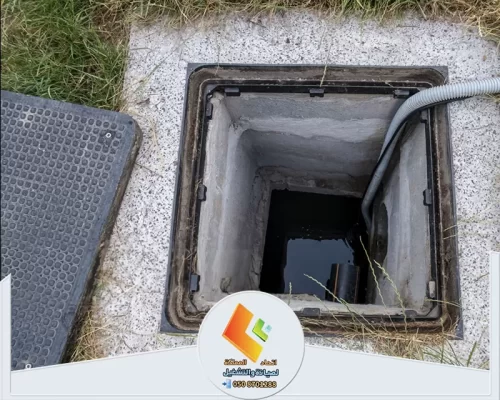فتحة صرف أرضية مفتوحة يظهر بداخلها تجمع مياه مع خرطوم ممتد إلى داخل المجرى لتنفيذ أعمال التنظيف.